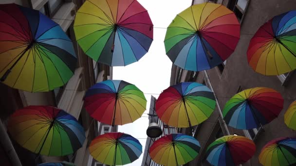 Veel kleurrijke regenboog open paraplu 's hangen over smalle straat tussen huizen - Video