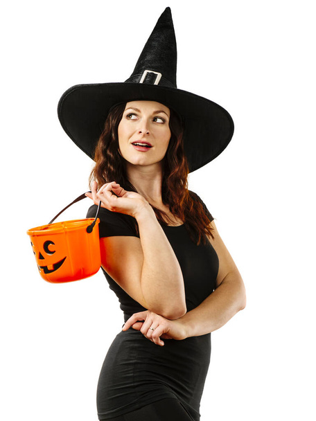 Young sexy redhead woman in witch hat and holding a pumpkin candy bucket for Halloween theme. - Foto, Imagem