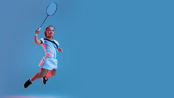 Mooie dwerg vrouw oefenen in badminton geïsoleerd op blauwe achtergrond in neon licht - Foto, afbeelding