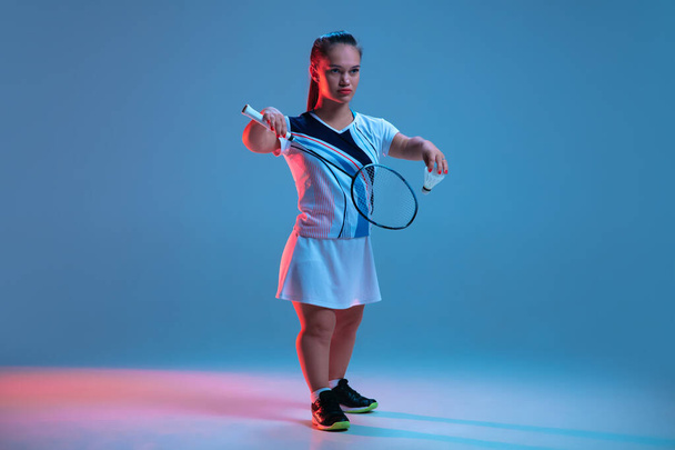 Beautiful dwarf woman practicing in badminton isolated on blue background in neon light - Фото, изображение