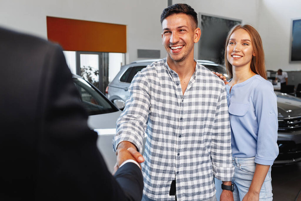 Cherrful young couple at the dealership buying a new car - Foto, Imagen