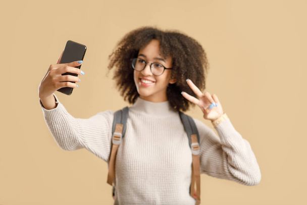 Selfie für Blog und zurück in die Schule. Lächelnde junge Amerikanerin mit Brille und Rucksack zeigt Frieden - Foto, Bild