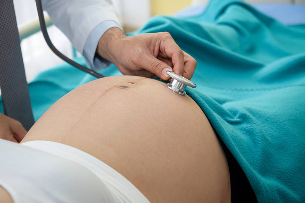 Lääkäri käytti kellon muotoista stetoskooppia tarkistaakseen klinikan sängyssä makaavan naisen raskauden.. - Valokuva, kuva