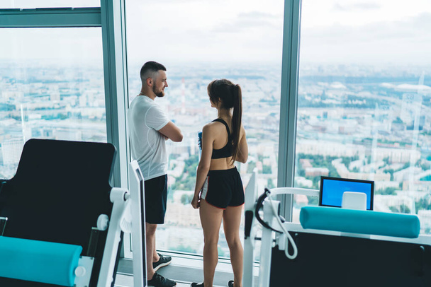 Rear view of caucasian male instructor talking to his female client during break on training for keeping perfect body shape, young woman and man couple in love having workout together for slimming - Foto, immagini