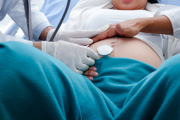 Profesyonel doktorlar, doğum yapmak üzere olan hamile kadınları kontrol etmek için steteskopu tutmak için eldiven takarlar.. - Fotoğraf, Görsel