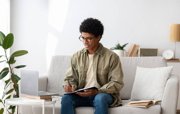 Etäopetuksen käsite. Keskittynyt musta opiskelija opiskelee etänä kannettavan tietokoneen kotona - Valokuva, kuva