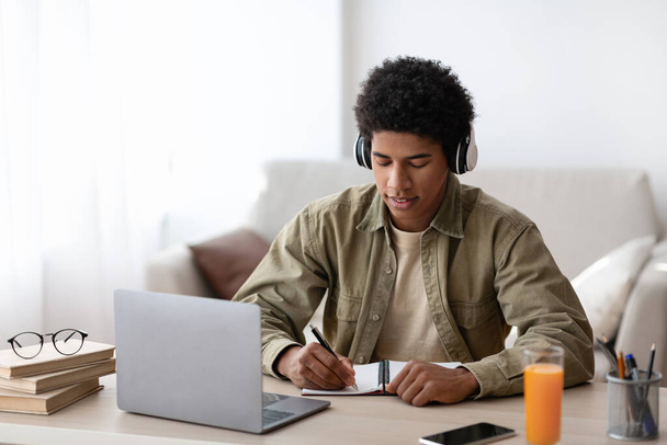 Otthonról tanulok. Afrikai amerikai tinédzser srác fülhallgatóval leírja info során online előadás zárt - Fotó, kép