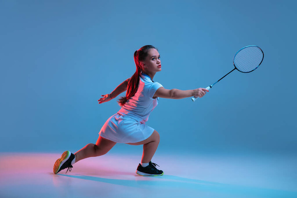 Beautiful dwarf woman practicing in badminton isolated on blue background in neon light - Photo, Image