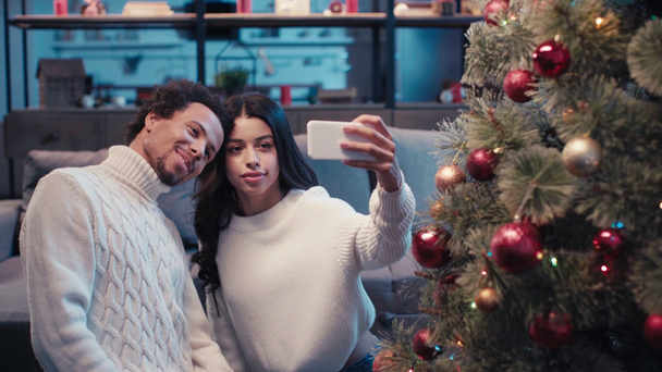 feliz africano americano pareja tomando selfie cerca de árbol de Navidad - Metraje, vídeo