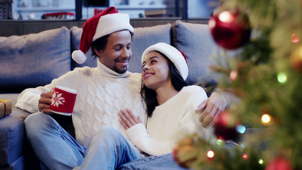 Afroamerikaner hält Tasse in der Hand und lacht mit Frau am Weihnachtsbaum - Filmmaterial, Video
