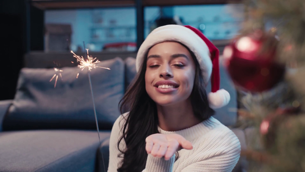happy african american woman in santa hat holding sparkler and sending air kiss - Felvétel, videó