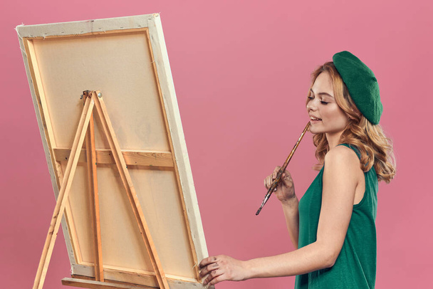 Frau Künstler grüne Baskenmütze Staffelei Pinsel Zeichenunterricht Kunst rosa Hintergrund - Foto, Bild