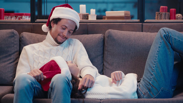 happy african american woman resting on couch near smiling man in santa hat - Footage, Video