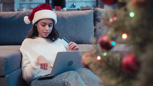 Afrikai amerikai nő kezében hitelkártya és a laptop közelében karácsonyfa - Felvétel, videó