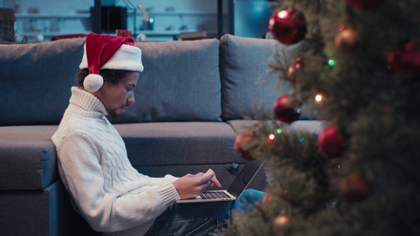Αφροαμερικανός άνδρας σε Σάντα καπέλο online ψώνια για τα Χριστούγεννα  - Πλάνα, βίντεο