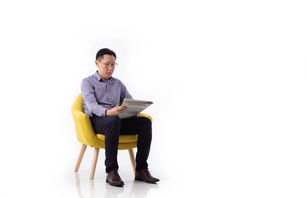 Un Asiatique assis dans un fauteuil lisant un journal isolé sur fond blanc - Photo, image
