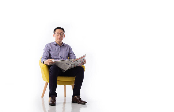 Um homem asiático sentado em uma poltrona lendo um jornal isolado no fundo branco - Foto, Imagem