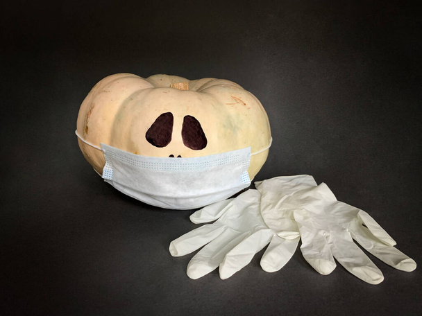 Sicheres Halloween 2020 während der Coronavirus-Pandemie. Halloween-Kürbis mit Mundschutz und Handschuhen - Foto, Bild