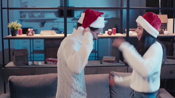 vrolijk Afrikaans amerikaans paar in rood santa hoeden dansen thuis - Video