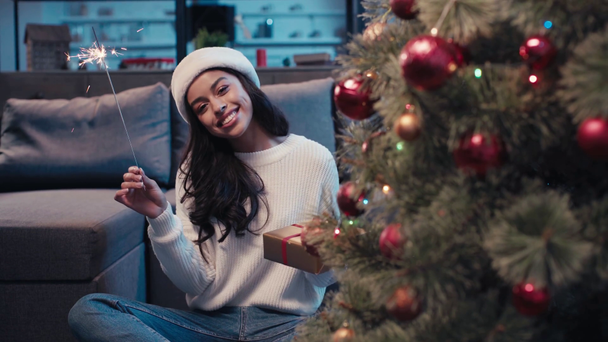 focus pull of happy african american woman holding sparkler and christmas gift - Séquence, vidéo