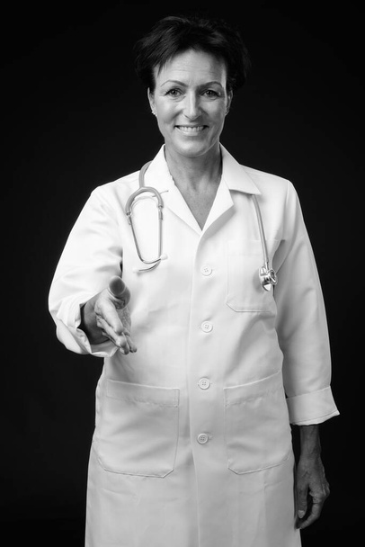 Estudio de maduro hermosa mujer escandinava médico con pelo corto sobre fondo negro en blanco y negro - Foto, imagen