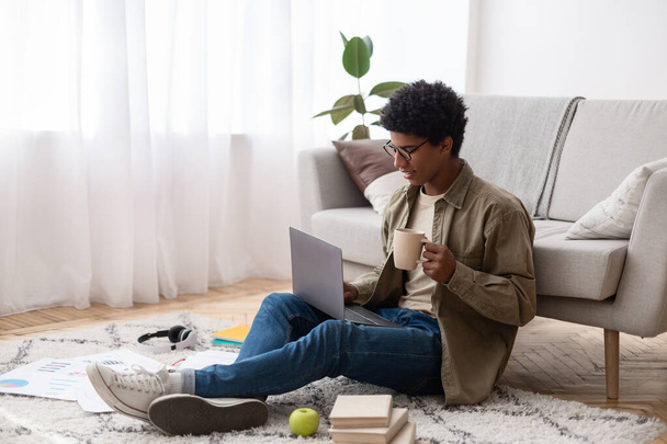 Atractivo adolescente negro usando el ordenador portátil y beber café durante sus estudios en línea en casa, espacio de copia - Foto, Imagen