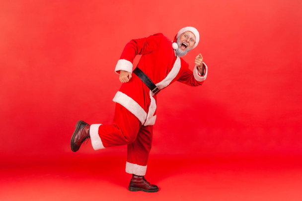 Full length excited happy santa claus running watching on you and pointing finger, merry christmas and happy new year. Indoor studio shot isolated on red background - Zdjęcie, obraz