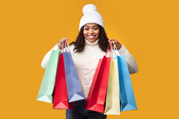 Smiling black woman showing shopping bags at studio - Foto, imagen