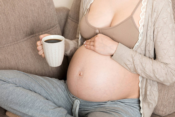 ragazza incinta seduta sul divano con tazza di caffè in caffè in mano. mattina di maternità. - Foto, immagini