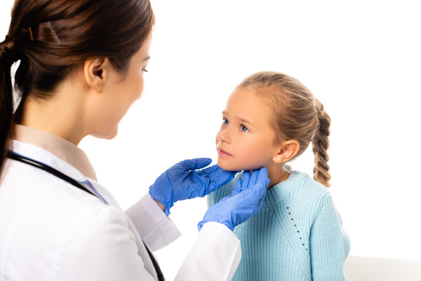 Selective focus of pediatrician in latex gloves touching neck of girl isolated on white - Fotó, kép
