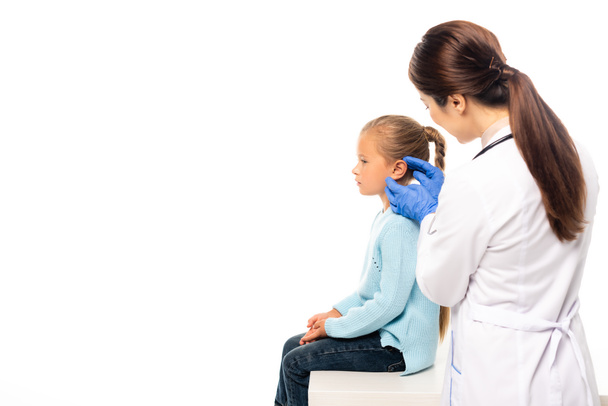 Селективный фокус педиатра в латексных перчатках, касающихся уха ребенка, изолированного на белом - Фото, изображение