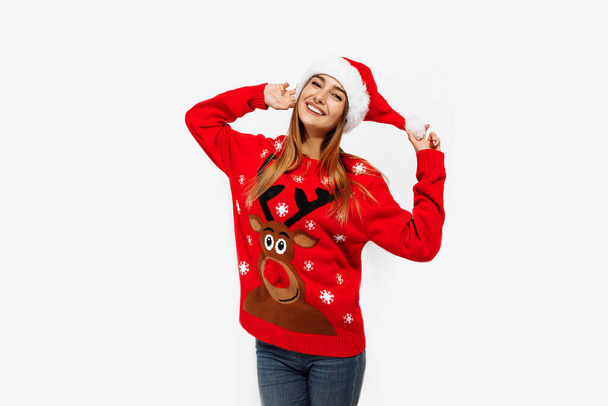 Happy cute young woman in christmas sweater and santa claus hat, on white background - Fotoğraf, Görsel