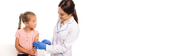 Panoramic shot of doctor in latex gloves touching hand of girl with patch isolated on white - Valokuva, kuva
