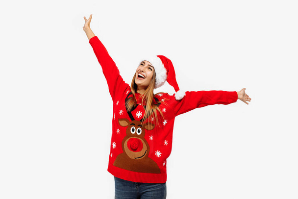 Excited young woman in christmas sweater and santa claus hat, having fun on white background - Фото, изображение