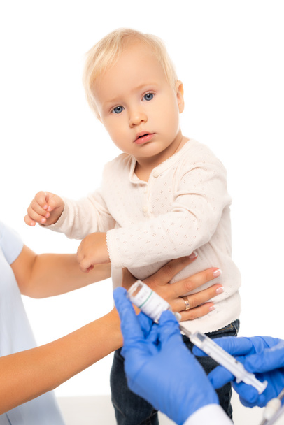 Селективный фокус малыша, смотрящего в камеру рядом с отцом и врачом со шприцем и вакциной, изолированной на белом - Фото, изображение