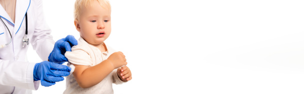 Horizontale Ernte von Arzt in Latex-Handschuhen hält Baumwolle in der Nähe der Hand von Kleinkind Junge isoliert auf weiß - Foto, Bild