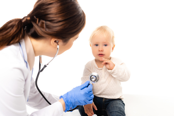 Selektive Fokussierung des Kleinkindes auf Kamera in der Nähe des Kinderarztes mit Stethoskop isoliert auf weiß - Foto, Bild