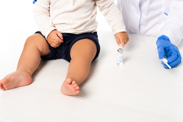 Vista recortada del médico sosteniendo la jeringa cerca del niño pequeño y el frasco con la vacuna aislada en blanco - Foto, Imagen