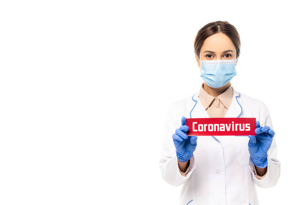Tıbbi maskeli doktor, beyaz harflerle izole edilmiş Coronavirus kartı tutuyor. - Fotoğraf, Görsel