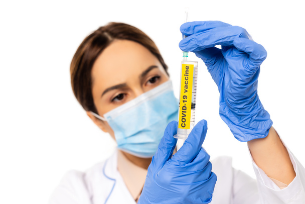 白い上に隔離されたcovid-19ワクチンレタリングとラテックス手袋保持注射器の医師の選択的な焦点 - 写真・画像