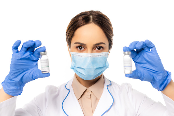 Doctor in medical mask and latex gloves holding jars with vaccine isolated on white - Фото, зображення