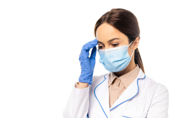 Médico en máscara médica y guante de látex tocando la frente aislado en blanco - Foto, Imagen