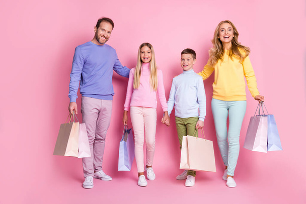 Full size photo of dream family mommy daddy two small kids hold shopping bags isolated over pink pastel color background - Фото, изображение