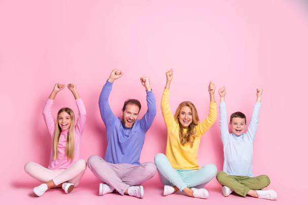 Full size photo of ecstatic dad mom and small girl boy sit with crossed legs raise fists isolated on pastel color background - Valokuva, kuva