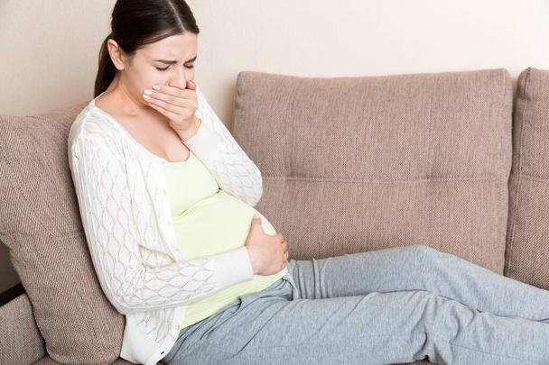 Embarazo por la mañana náuseas. Mujer embarazada teniendo náuseas sintiéndose mal en el sofá en el hogar. - Foto, Imagen