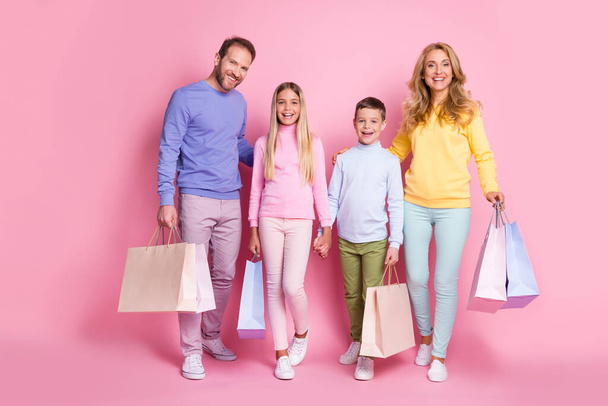 Full size photo of positive family dad mom two little kids hold shopping bags isolated on pink pastel color background - Fotó, kép