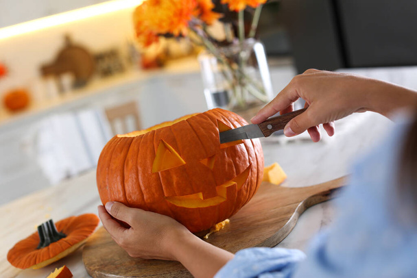 Woman making pumpkin jack o'lantern at table in kitchen, closeup. Halloween celebration - Photo, image