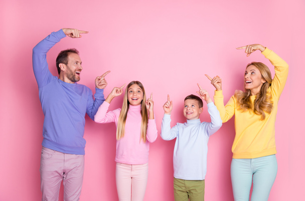 Foto van verrast moeder vader kleine kinderen wijzen index vinger omhoog lege ruimte geïsoleerd over pastel roze kleur achtergrond - Foto, afbeelding