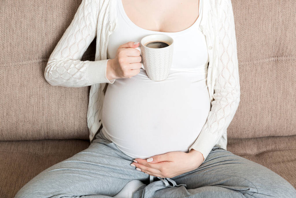 ragazza incinta seduta sul divano con tazza di caffè in caffè in mano. mattina di maternità. - Foto, immagini