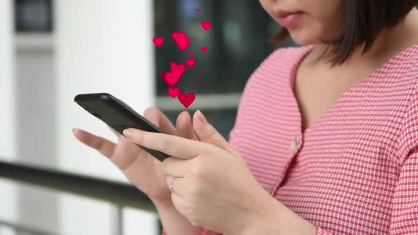 Азиатская красивая женщина использовать смартфон с красным значком сердца из экрана социальной сети. Расслабьтесь на открытом воздухе без маски для лица, но сохраняйте социальную дистанцирующуюся коронавирус новую нормальную концепцию. Психическое здоровье - Кадры, видео